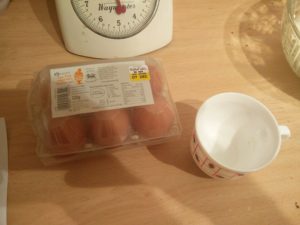 The pack of eggs and the cup to break them into